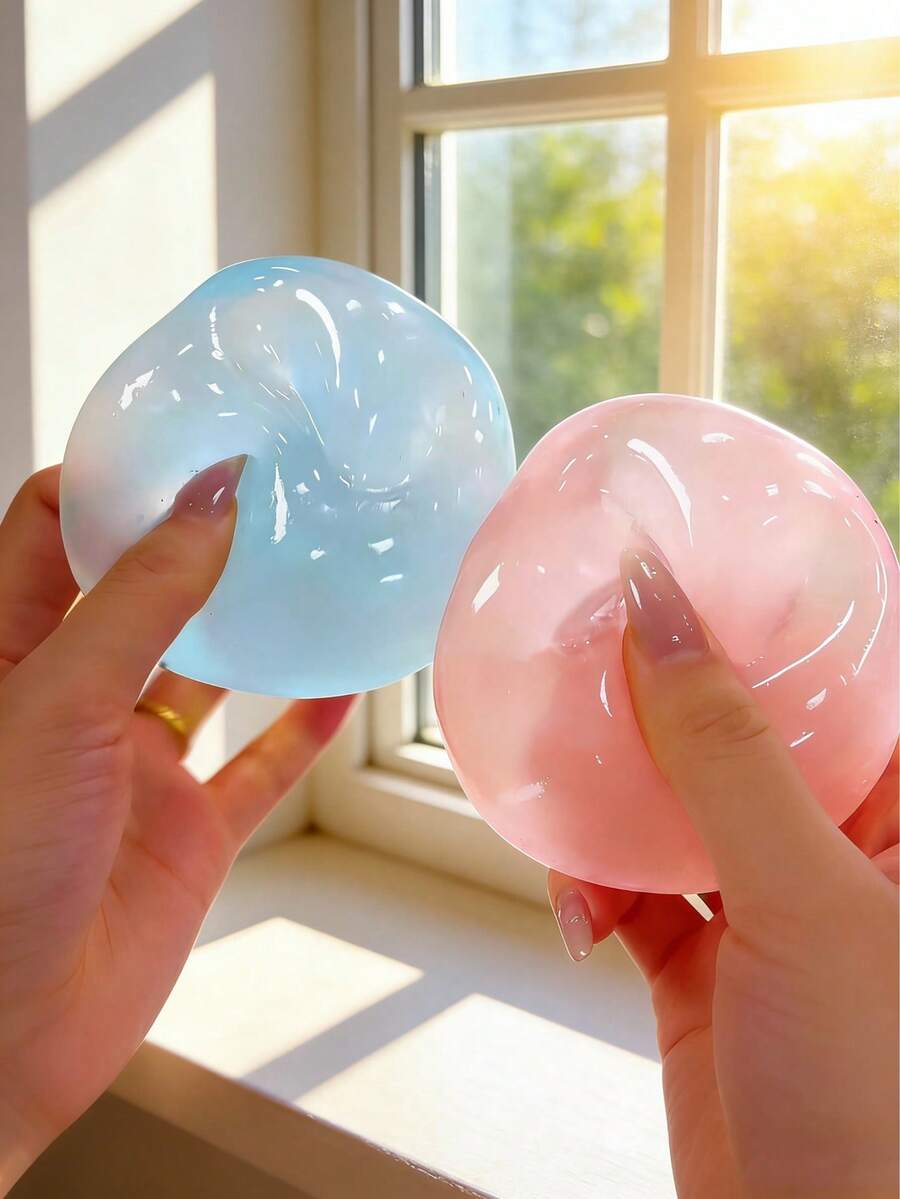 Deux balles antistress translucides et souples, bleu clair et rose, fabriquées en silicone, tenues délicatement dans des mains soignées pour l’utilisation de la balle compressible antistress à l’huile de coco bleue.