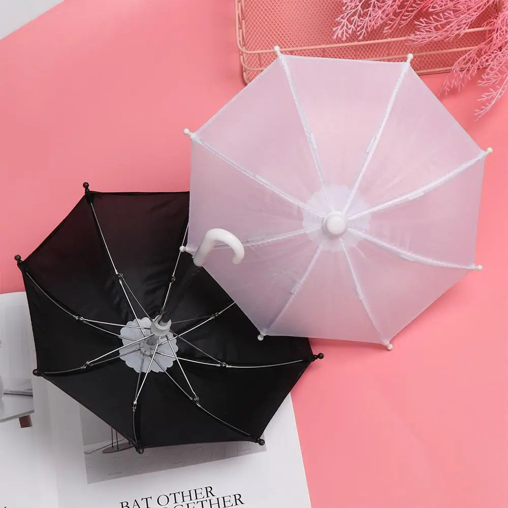 A delicate translucent white mini doll umbrella with a curved handle and matching white ribs rests beside a sleek black mini doll umbrella featuring silver metallic spokes, both designed as bjd accessories.