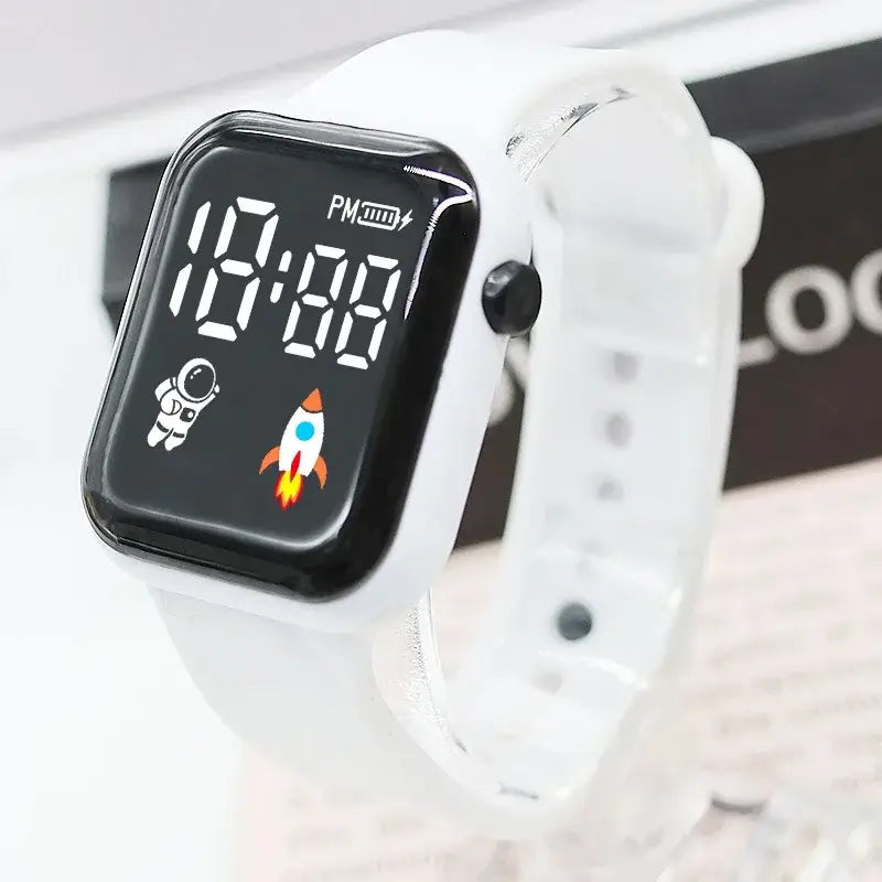 Montre électronique blanche pour enfants, garçons et filles, avec écran LED noir affichant un design d’astronaute et de fusée, et un bracelet en silicone blanc.
