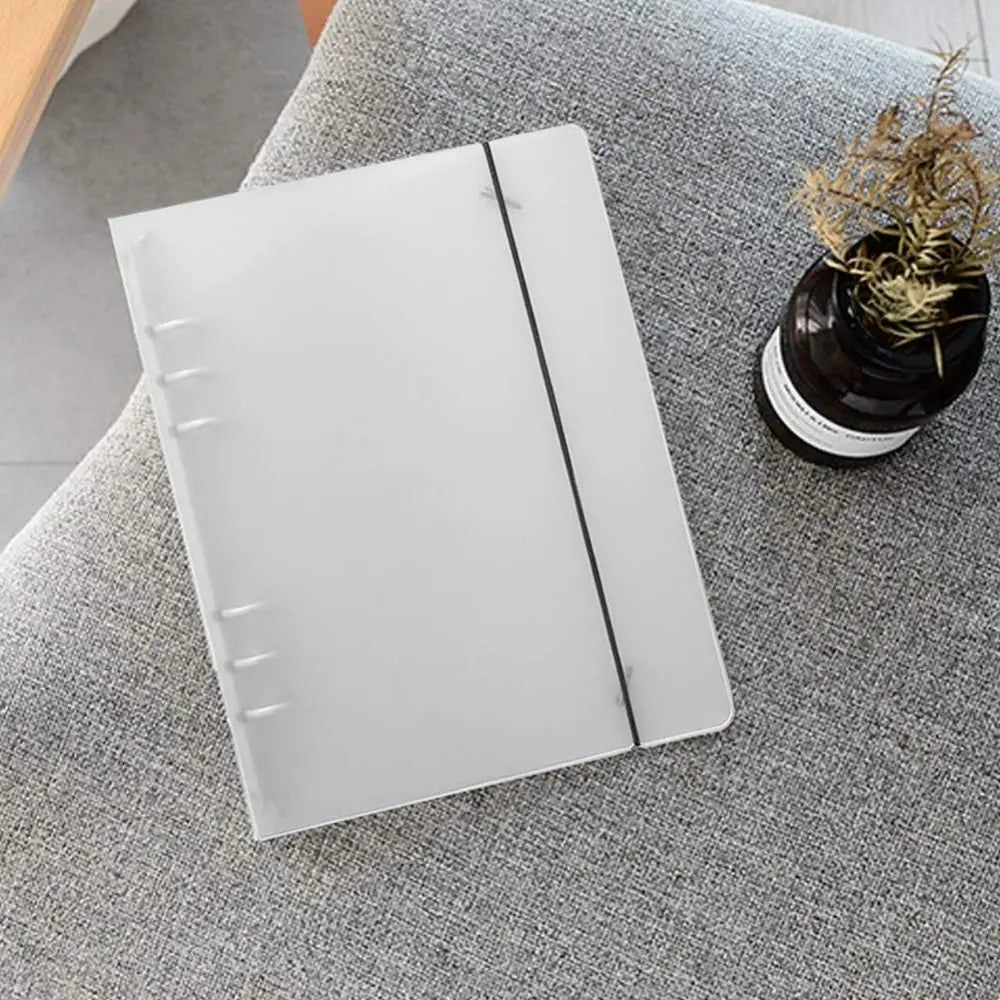 A minimalist white plastic A5 translucent loose leaf ring binder notebook featuring a black elastic band and three silver-colored ring clasps.