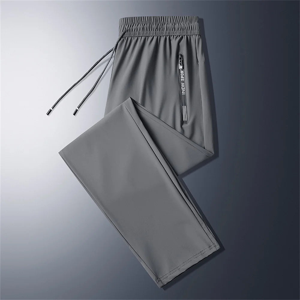 Jogger de hombre fitness 5XL en gris, con cintura ajustable mediante cordón y un bolsillo vertical con cremallera con nueva imagen de marca deportiva.