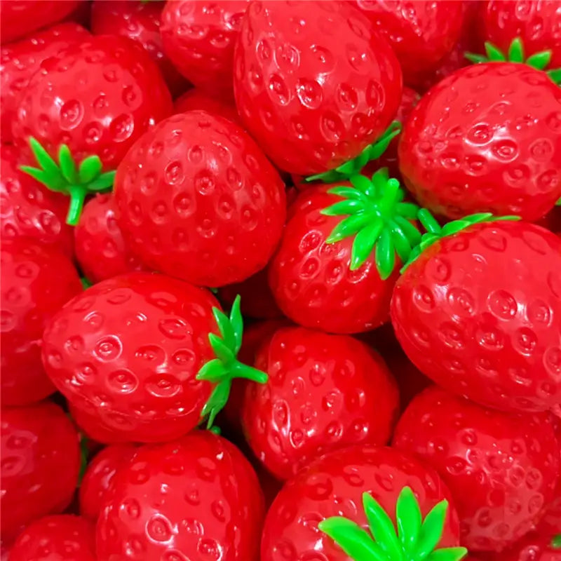 Fraises en plastique rouges aux couleurs vives, avec sommets verts feuillus, présentées comme jouet sensoriel de type balle anti-stress en forme d’arachide.