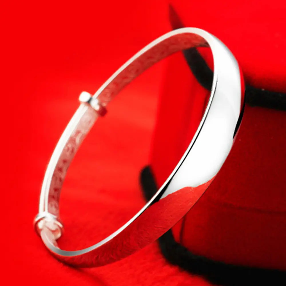Sterling silver round bangle bracelet for women with a sleek silver-toned polished exterior and an engraved inner band.