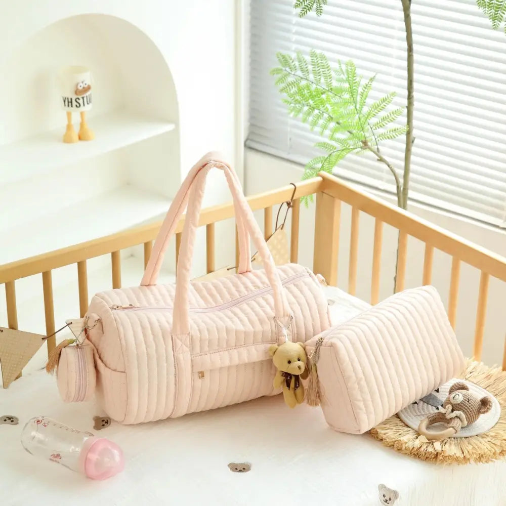 Eine zartrosa gepolsterte Kinderwagen-Organizer-Tasche aus robustem Stoff mit passenden Tragegriffen und einem kleinen Teddybär-Anhänger, der seitlich herabhängt.