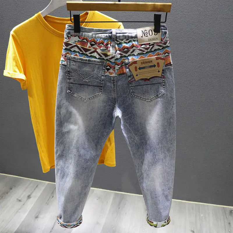 Men slim fit stretch white denim jeans featuring light-wash fabric with a colorful geometric pattern along the waistband and rolled cuffs, adorned with a n09 design label.