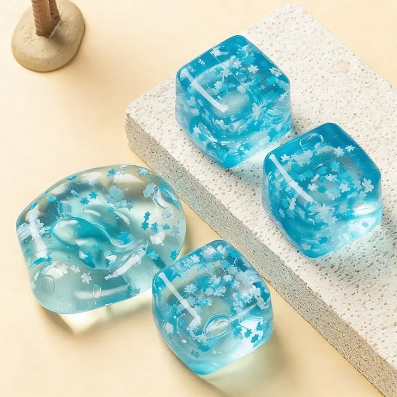 Translucent blue resin ice cubes with embedded white floral patterns designed as slow rising sensory fidget toys.