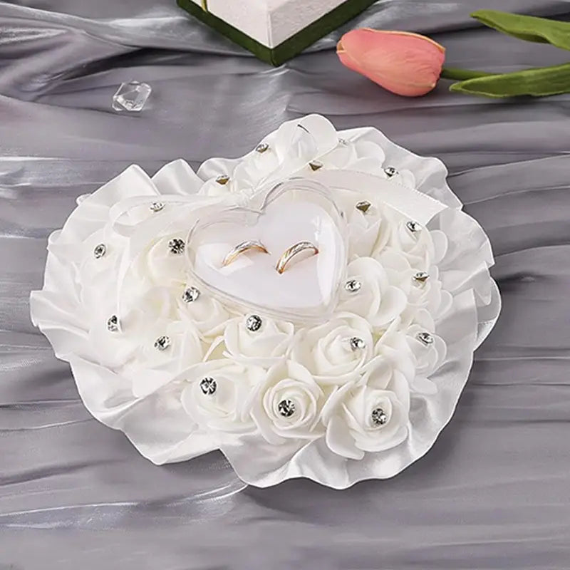 ハート型の収納部に2つのゴールドリングを収める白いフローラルのラインストーン結婚指輪リングピロー（ブライダルブーケ用）。