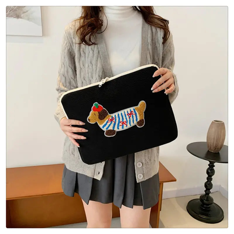 Schwarze Kord-Laptophülle für MacBook Pro mit einem farbenfrohen bestickten Dackel, der in gestreifter Kleidung einen Apfel hält.