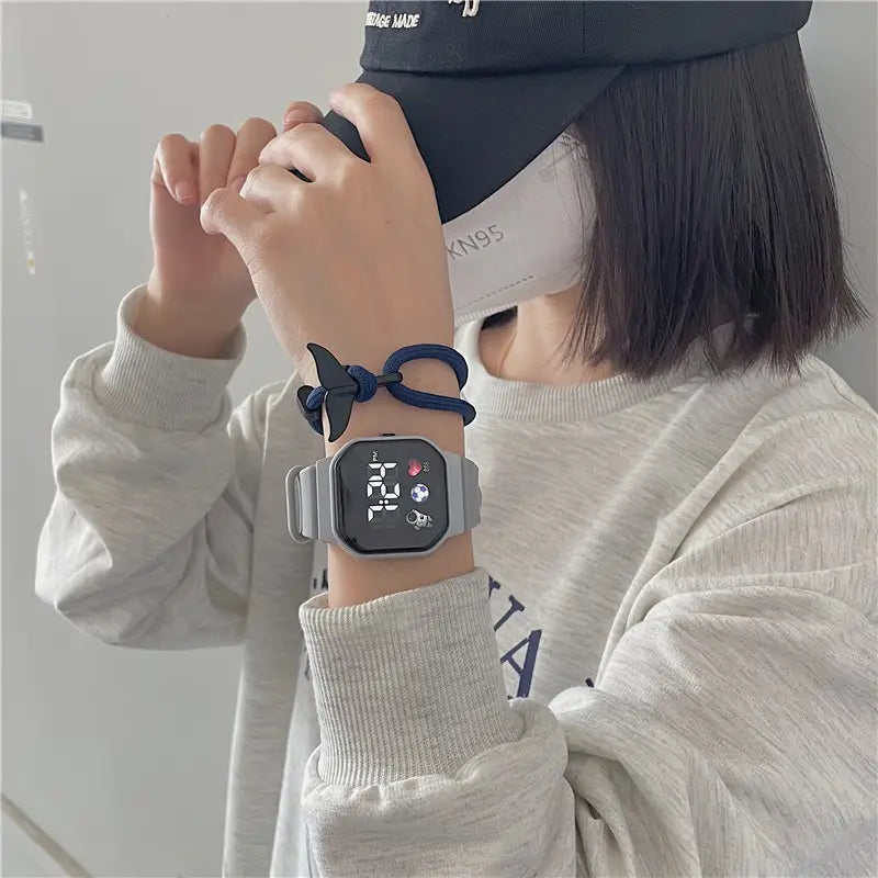 グレーのキッズ用LEDデジタルスポーツウォッチ。正方形のフェイスと、防水シリコーンバンド。ネイビーブルーの編み込みコードブレスレットとセットです。