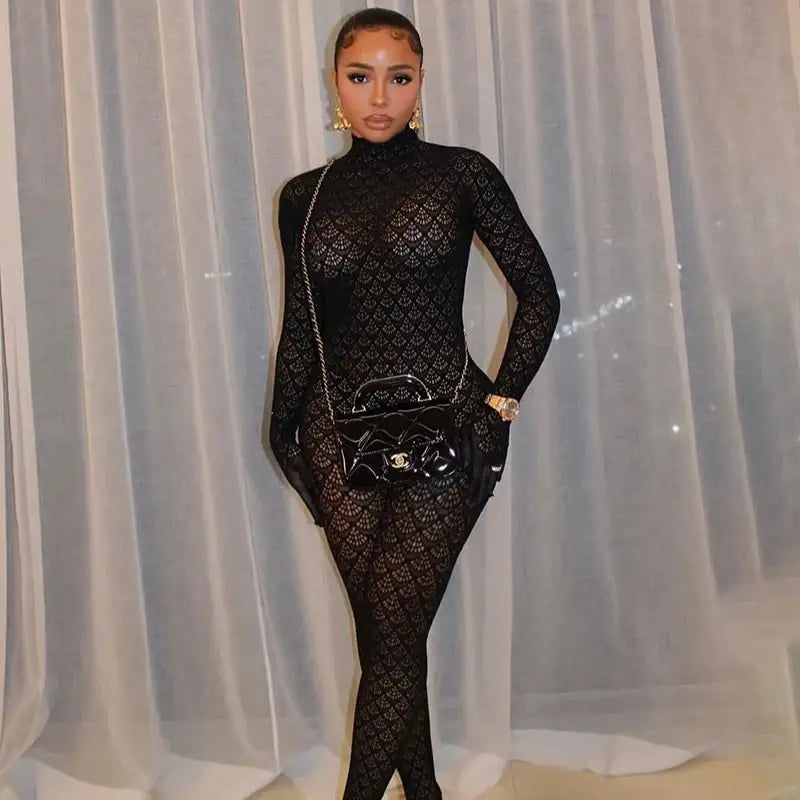 Black glossy Chanel handbag with chain strap and metallic hardware paired with a fishnet see through long romper.