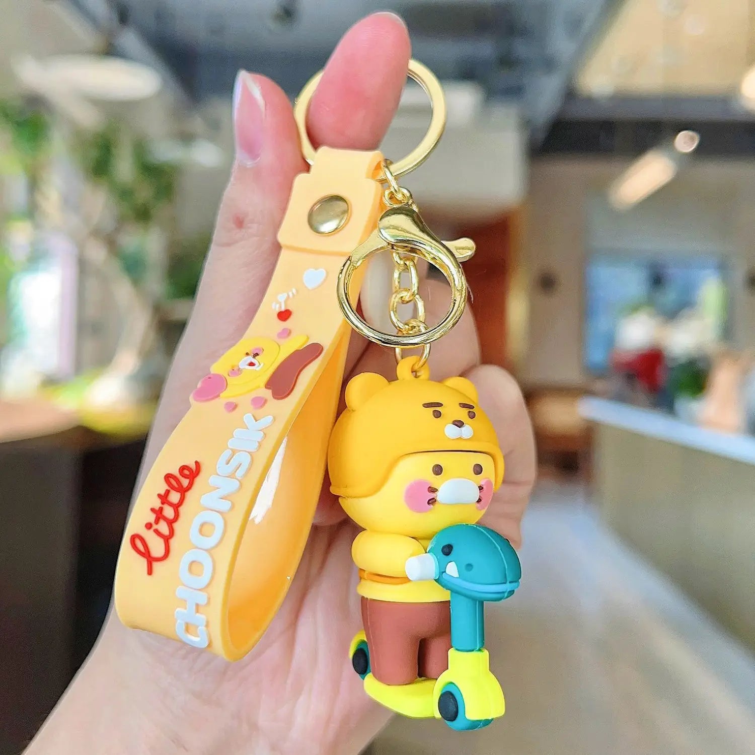 Yellow choonsik silicone keychain featuring a cartoon bear holding a scooter and the text little choonsk on the strap, a Korean viral gift.