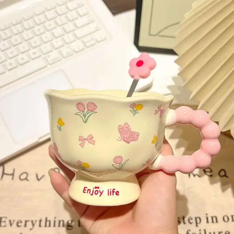 Tasse tulipe en céramique de couleur crème avec anse rose perlée et décors floraux de papillons, comprenant une cuillère assortie en forme de fleur rose dans une boîte cadeau à motif floral.