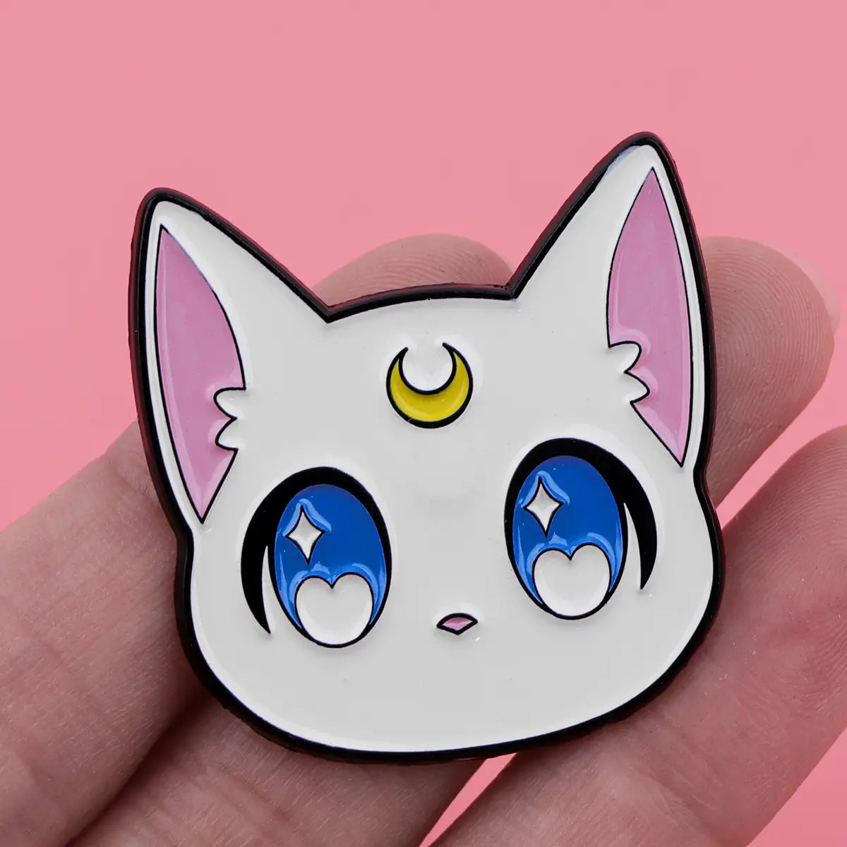 「セーラームーン」猫のエナメルピンセットより、かわいらしい猫の顔をモチーフにした白いエナメルピンであり、ピンクの内耳、青いきらめく目、そして額の黄色い三日月が特徴です。