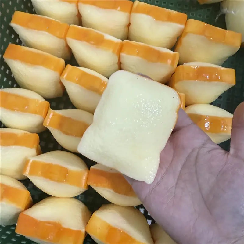 Eine Hand hält einen eckigen, offweiß- und orangefarbenen, geschichteten Butterstick als ASMR-Sensory-Squishy-Spielzeug mit glänzendem Finish.
