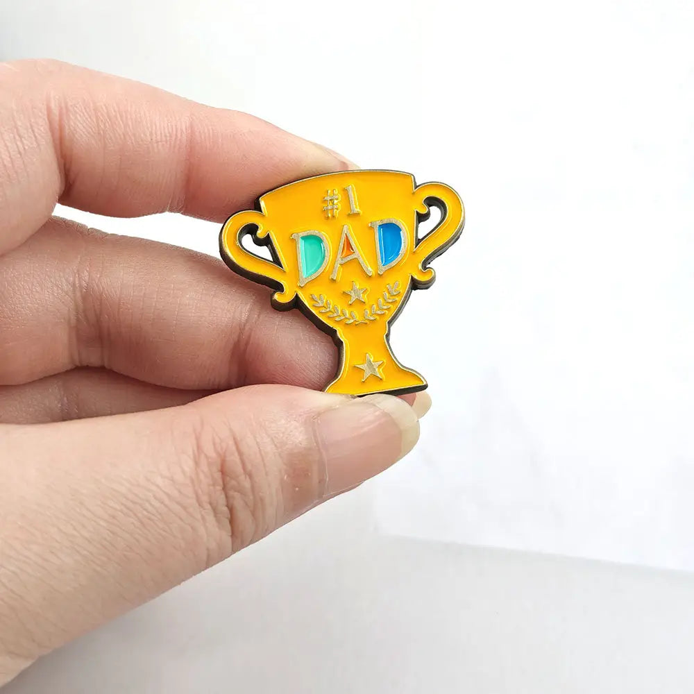 Produit : broche en émail doré brillante en forme de trophée avec des lettres « number one dad » en bleu et turquoise, rehaussées de petits accents en forme d’étoile sur une broche dorée en émail de trophée « number one dad ».