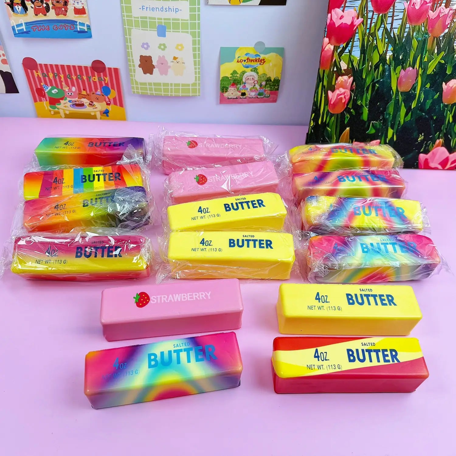 Jouet antistress souple à la forme de beurre à la fraise à montée lente, présentant des bâtonnets de beurre au motif arc-en-ciel coloré, dans un emballage en plastique transparent, avec des étiquettes jaunes imprimées du mot « beurre ».