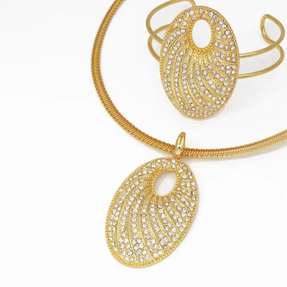 Collar de novia chapado en oro con pedrería y una cadena trenzada en tono dorado, con un colgante ovalado que presenta intrincados patrones similares a plumas engastados con cristales transparentes.