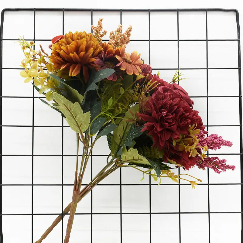 鮮やかな秋をテーマにした造花のバラのウェディングブーケで、濃いオレンジ、深い赤、柔らかなイエローの色合いに層をなす花びらが特徴で、緑の葉物があしらわれています。