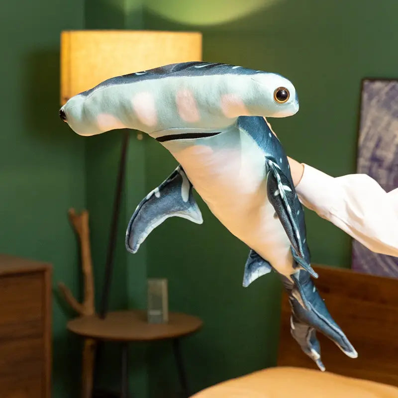 A plush hammerhead shark plush pillow soft toy with a light blue and white body, dark gray fins and head markings, and a brown eye.