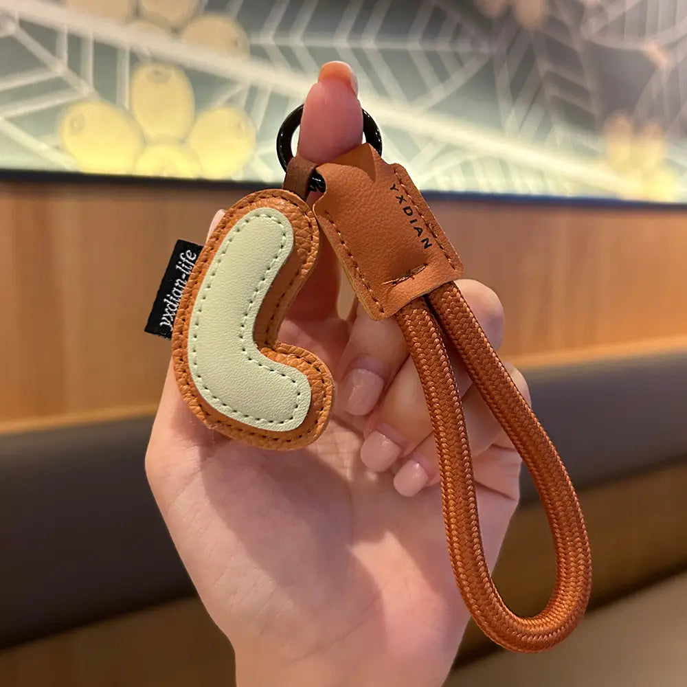 A tan leather initial keychain letter wristband charm with a light green stitched phone-shaped charm and an orange braided strap.