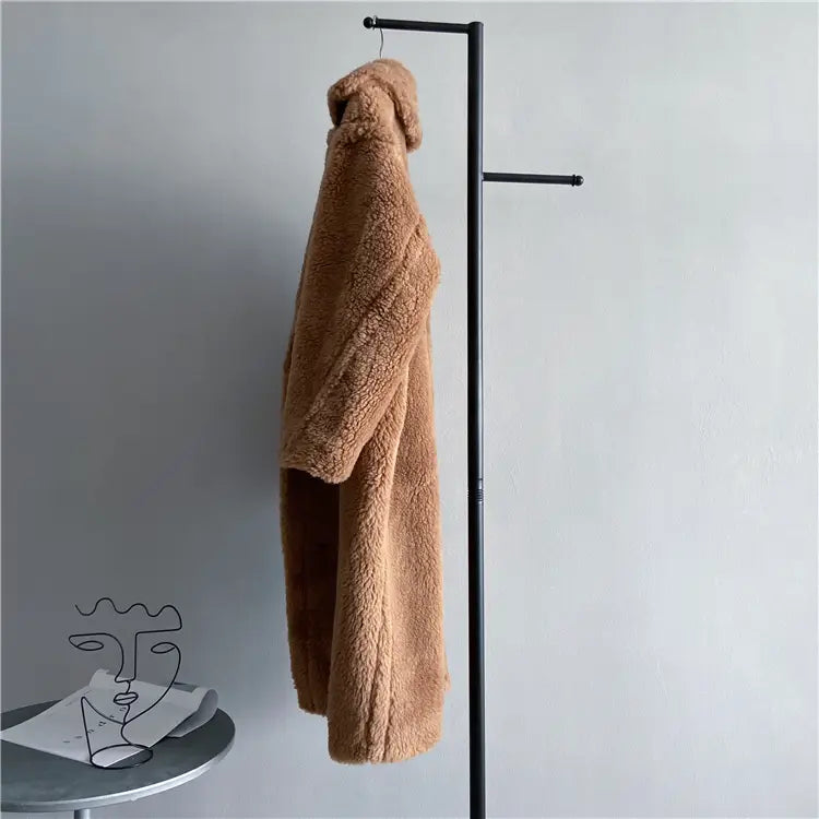 Abrigo exterior tipo osito de peluche largo para mujer de lana en color beige claro, esponjoso, colgado ordenadamente en un perchero de ropa metálico negro, destacando el contorno de pecho y el contorno de cadera para asistencia del servicio de atención al cliente.