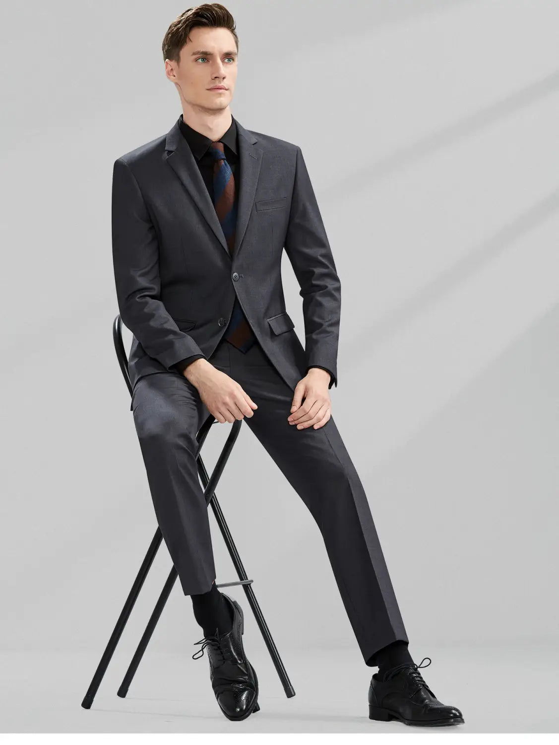 Costume gris foncé élégant pour homme en coupe slim, coupe ajustée et léger éclat, avec un type de fermeture boutonnée simple, adapté aux tenues formelles et professionnelles décontractées.
