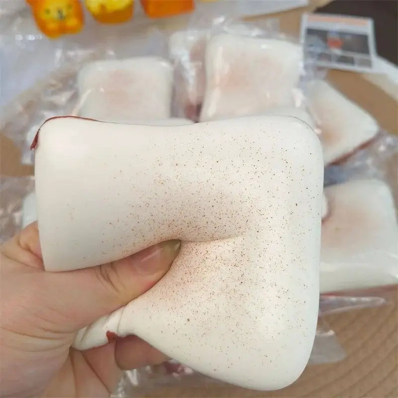 Jouet anti-stress en forme de toast moelleux blanc tacheté, couleur macaron, avec une texture souple et extensible et un détail de fermeture éclair rouge.