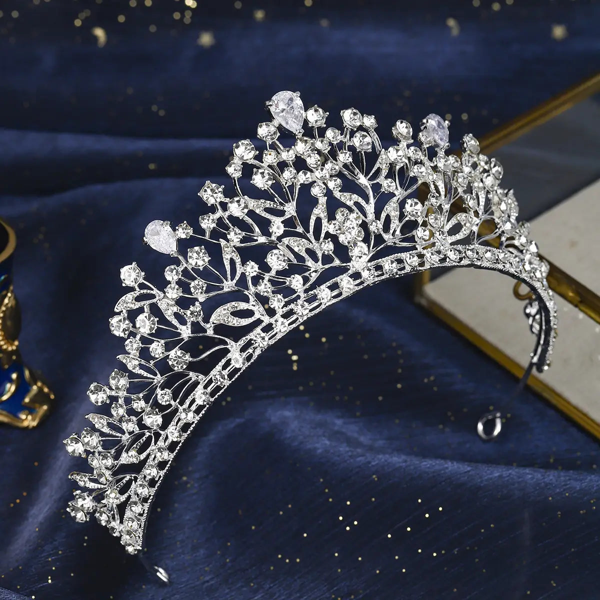 Une tiare de mariage en cristal d'argent étincelant, avec des motifs complexes de feuilles et de vignes, et de nombreux cristaux transparents, y compris des pierres plus grandes en forme de poire, pour un usage lors du mariage.