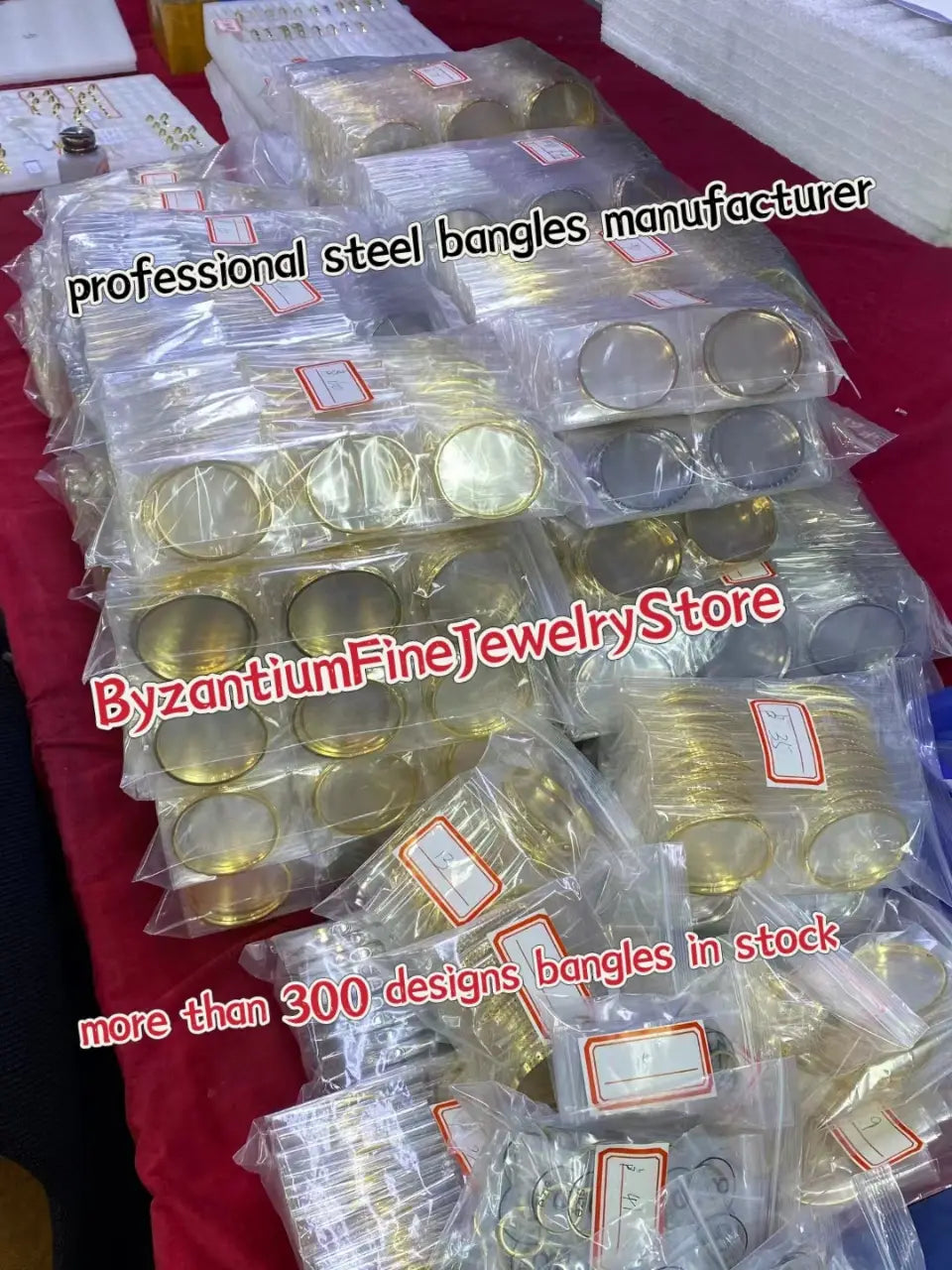 Gold- und silberfarbene Armreifen aus Stahl in transparenter Kunststoffverpackung, die in einem Juweliergeschäft neben dem Produkt „Ohrringe mit silbernen Tropfenquasten in Gold-Vermeil“ ausgestellt sind.