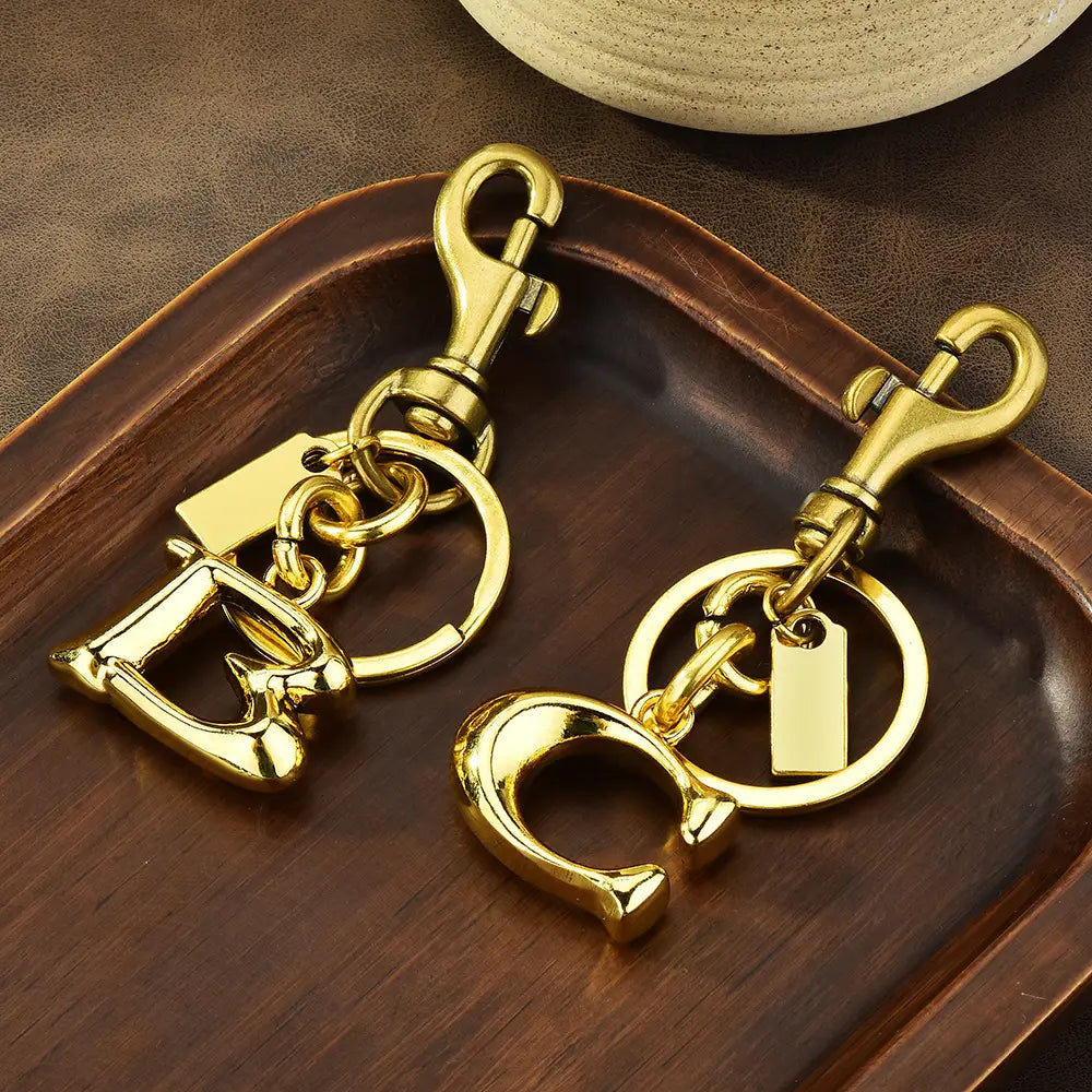 Gold-tone metal keychain with a polished finish featuring letter d and c charms attached to circular rings and swivel clasps designed as a car accessory.