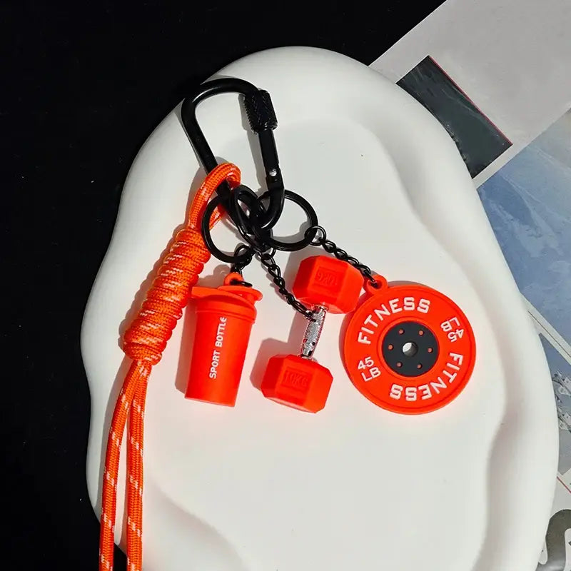 Porte-clés de musculation en silicone orange éclatant comprenant une breloque de disque de poids pour haltère et une breloque de bouteille shaker, en tant qu’article-cadeau.