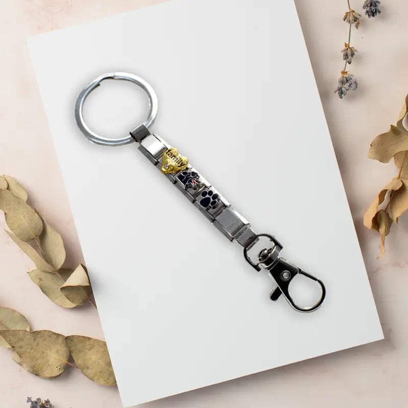 Llavero con dije de eslabones italianos de metal personalizado en bricolaje, color plata, con un dije de familia en color dorado y dijes de huella de pata negros.