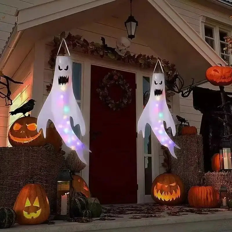 two glowing white inflatable halloween ghosts with black facial features and colorful led lights hanging as an outdoor windsock for home halloween ghost decoration