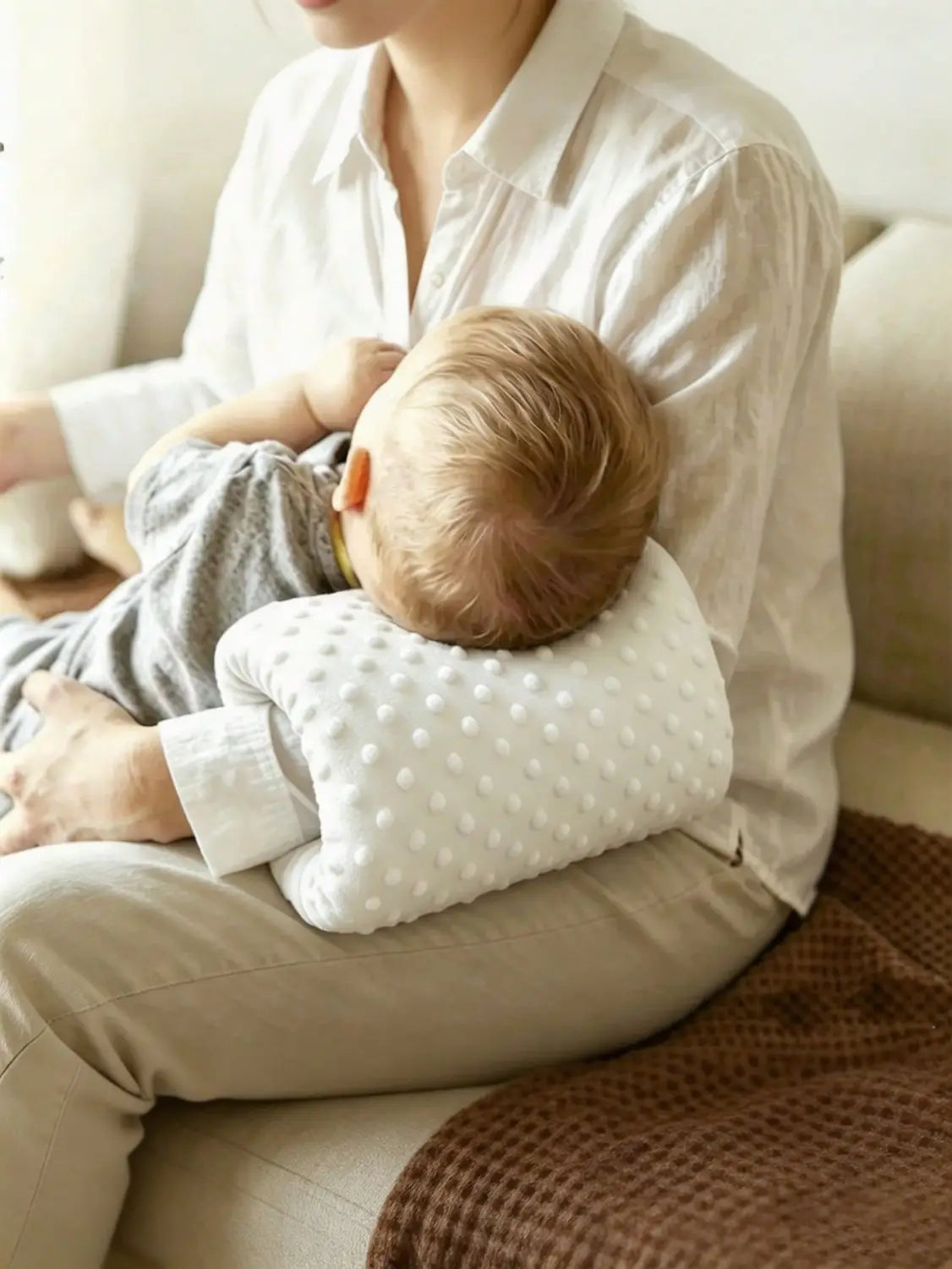 weißes strukturiertes Baby-Fütterungs-Armkissen mit weichen, abgerundeten Kanten und einem zarten Punktmuster, ausgelegt als weiches Stillstützkissen.