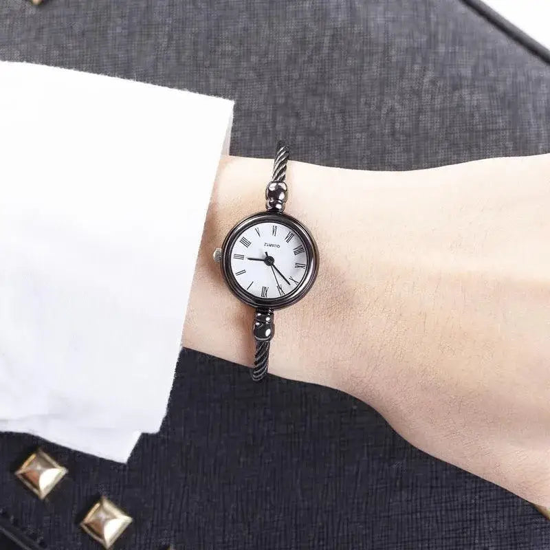 Black cable bracelet women stainless steel quartz bangle watch with white face and roman numerals.