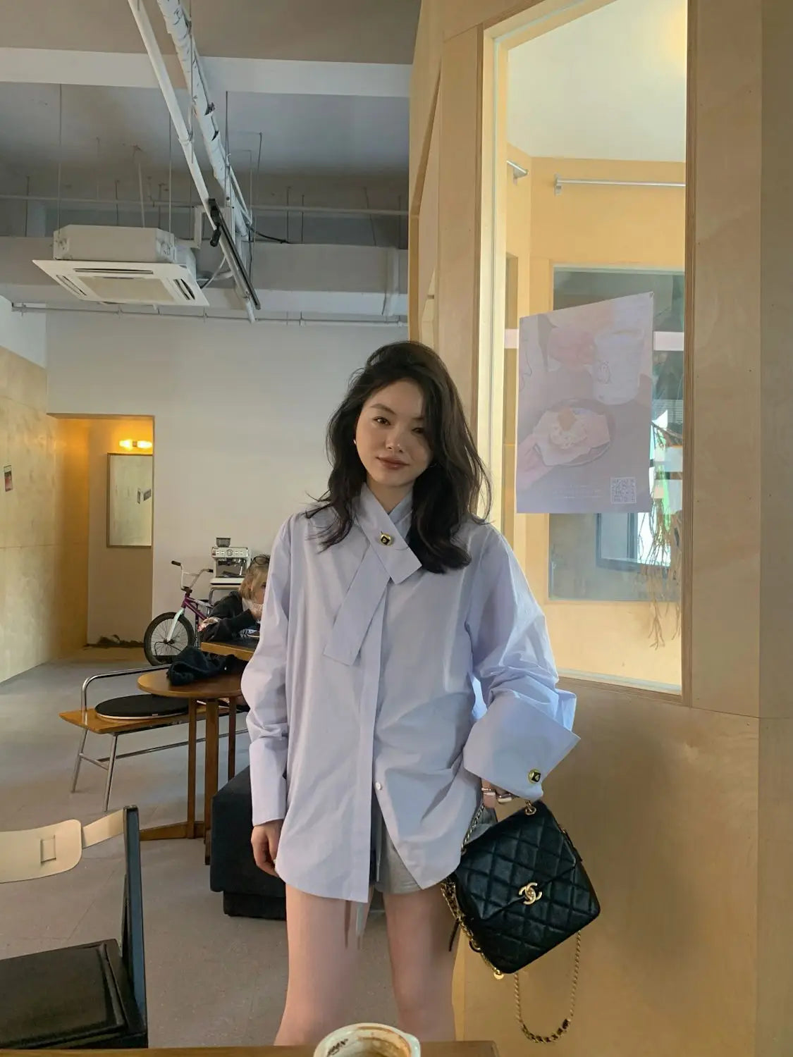 Black quilted leather Chanel handbag with gold-tone chain strap paired with a light blue oversized button up shirt.