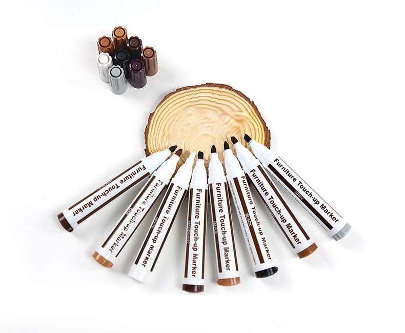 Set aus weißen und braunen Holz-Reparierstiften mit schwarzen Kappen, in Fächerform auf einem Holzstück angeordnet, für die Möbelreparatur und Holzkratzer.