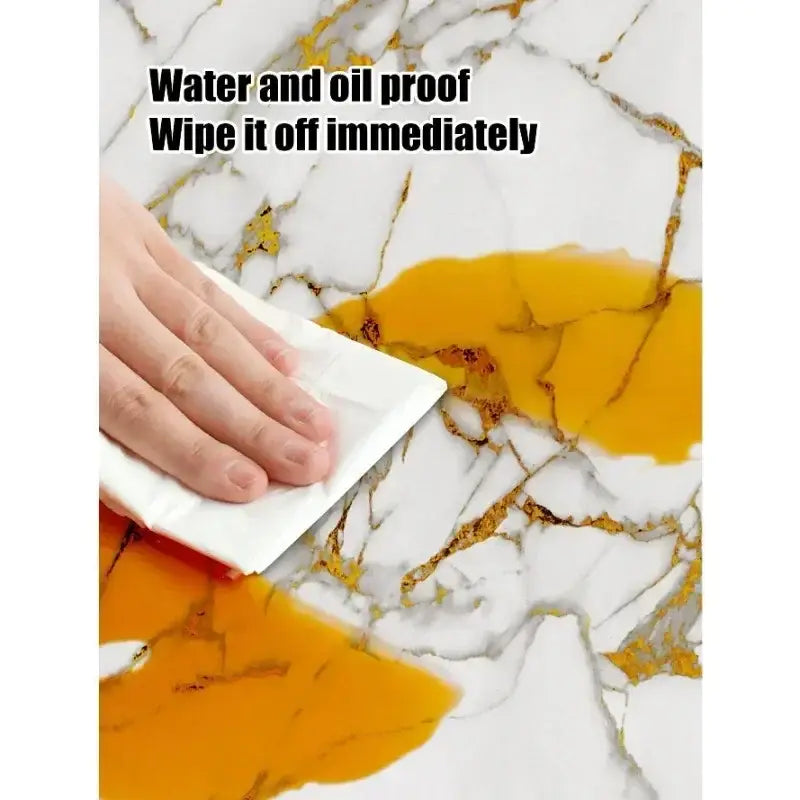 Toalla de papel blanca para limpiar un derrame sobre pegatinas de azulejos de mármol blanco y dorado con respaldo adhesivo a prueba de agua sobre una superficie de mármol.