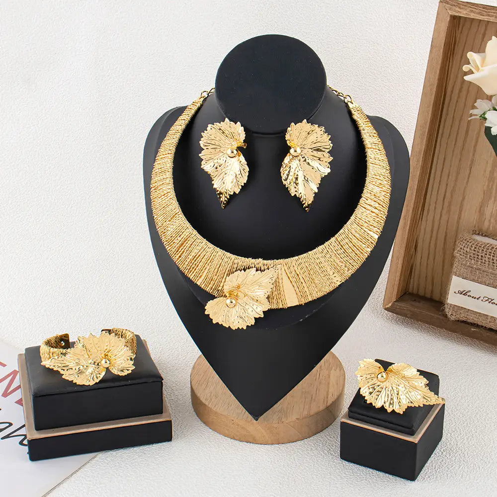 Parure de bijoux en perles et feuilles d’or, comprenant un collier statement, des boucles d’oreilles assorties, un bracelet et une bague, avec des détails métalliques dorés complexes.