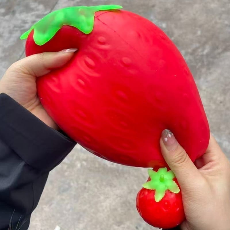 A vibrant red jumbo strawberry-shaped slow rising sensory fidget toy featuring a green leafy top and a smaller matching toy attached by string.