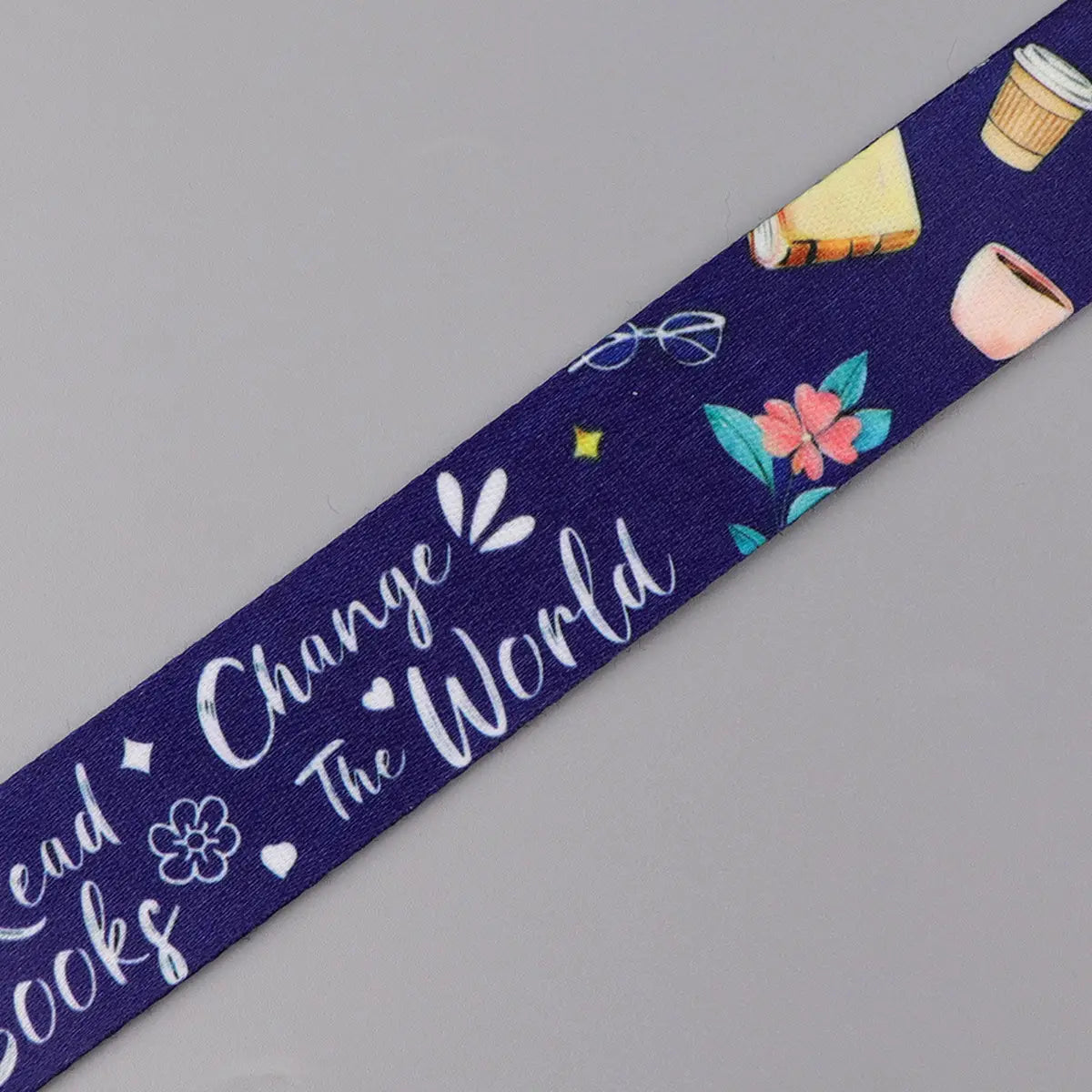 A navy blue woven book lover lanyard and ID card holder set featuring a playful pattern of coffee cups, books, glasses, flowers, and the phrase read.