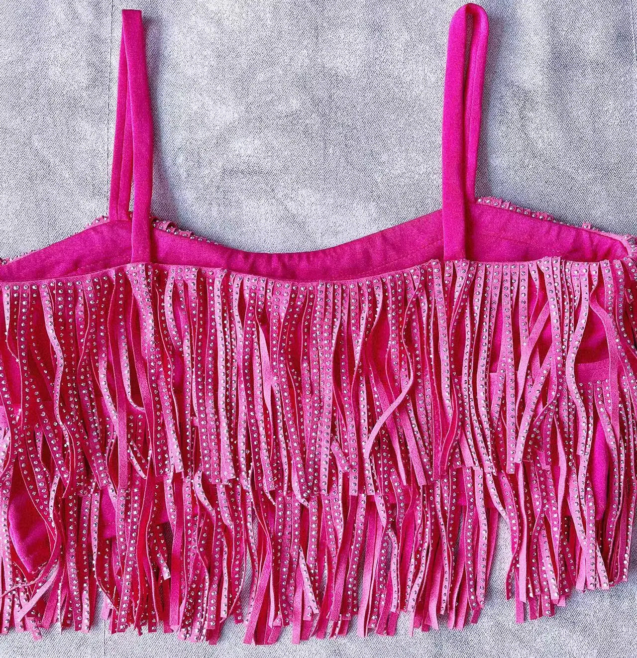Haut fuchsia à franges, avec fines bretelles et des détails en strass scintillants, assorti à une mini-jupe taille haute à franges en strass.
