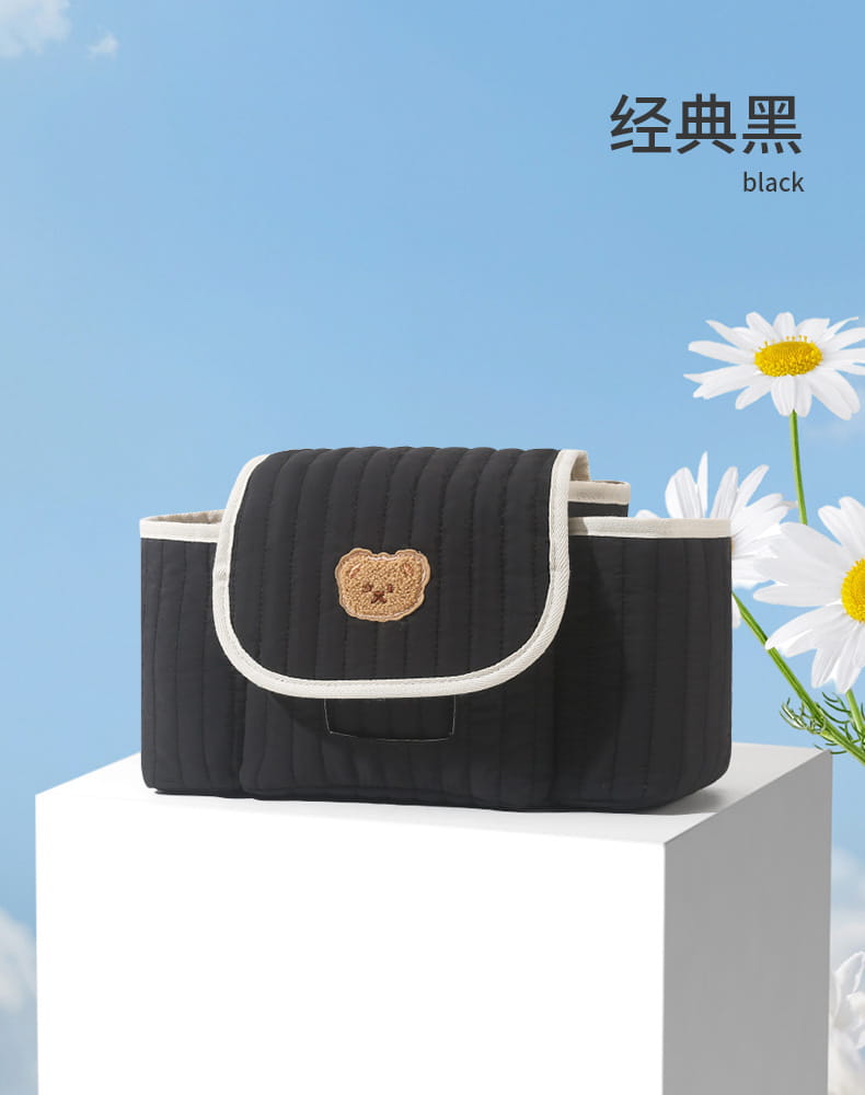Schwarze wattierte Wickeltasche für Babys mit beigefarbener bestickter Bären-Gesichtsstickerei und weißem Zierbesatz zur Verwendung als wattierter Kinderwagen-Organizer-Beutel.