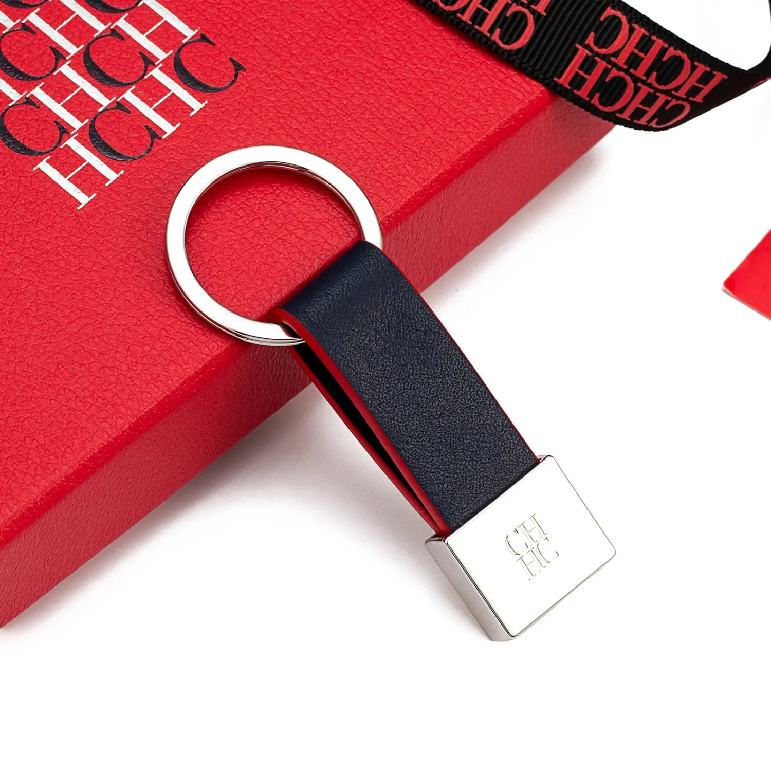 Porta llaves de cuero negro con anillo metálico plateado y una placa rectangular con el logotipo hch como accesorio de equipaje minimalista.