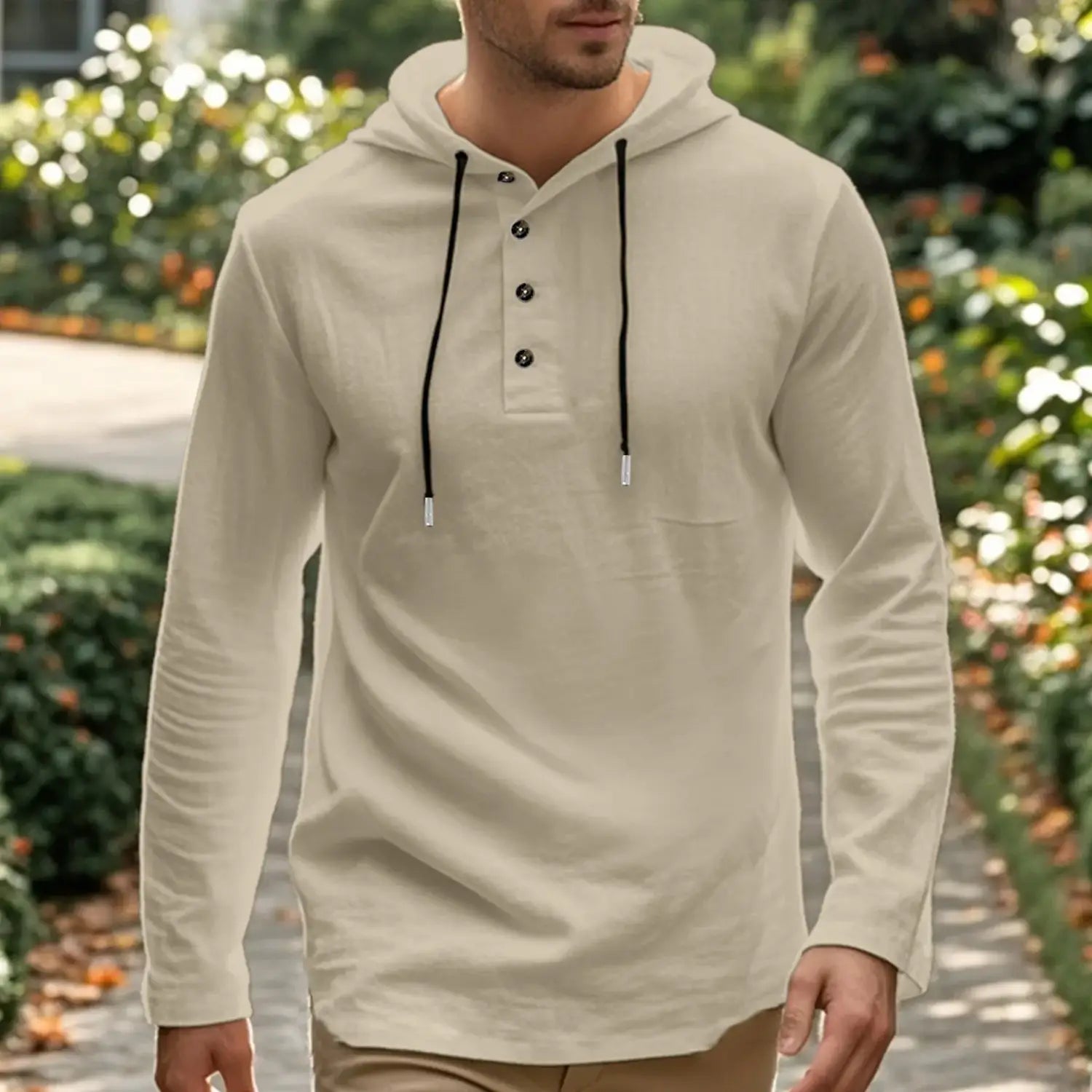 Cream-colored men cotton linen hooded henley shirt with long sleeves black drawstrings and button accents.