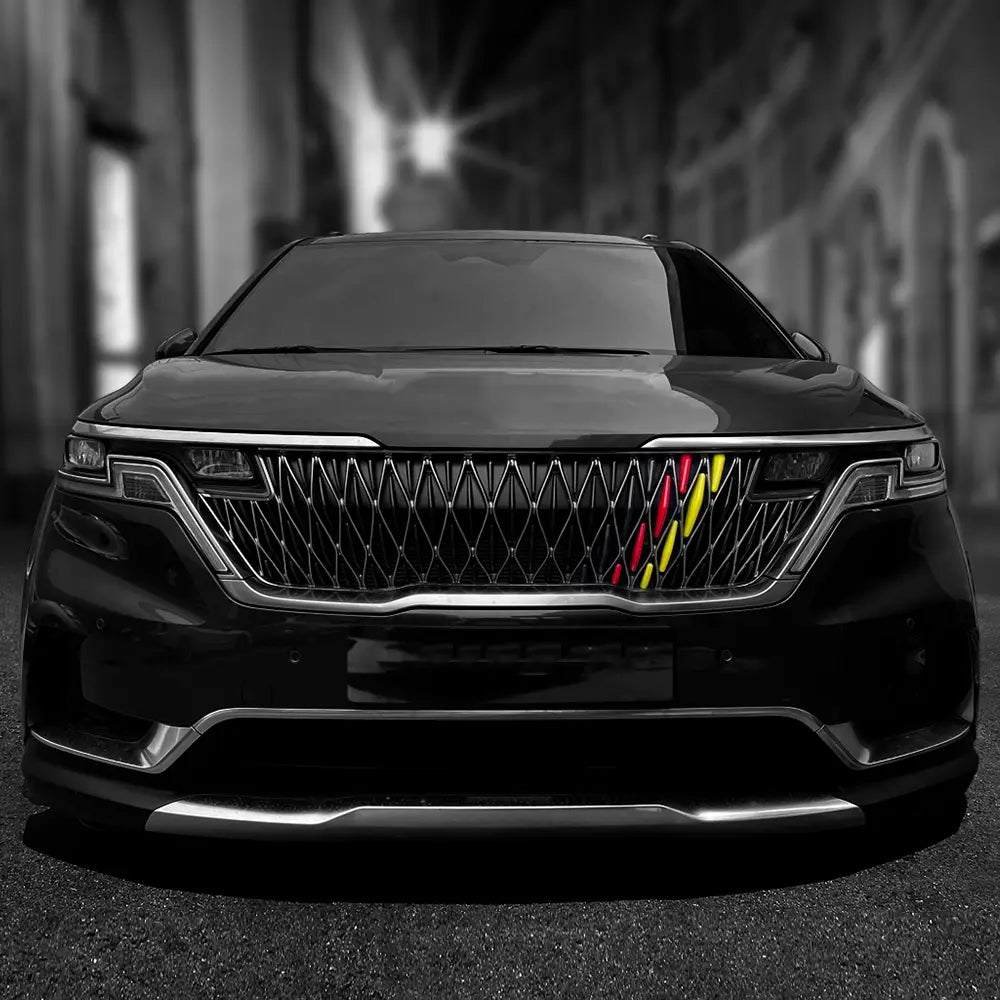Schwarzer SUV mit einer Kia Carnival Ka4 Frontgrill-Zierleiste aus ABS für die Jahre 2022–2024, mit einem markanten, diamantförmig gemusterten Kühlergrill, der mit kräftigen diagonal verlaufenden Streifen in Rot, Gelb und Grün akzentuiert ist.