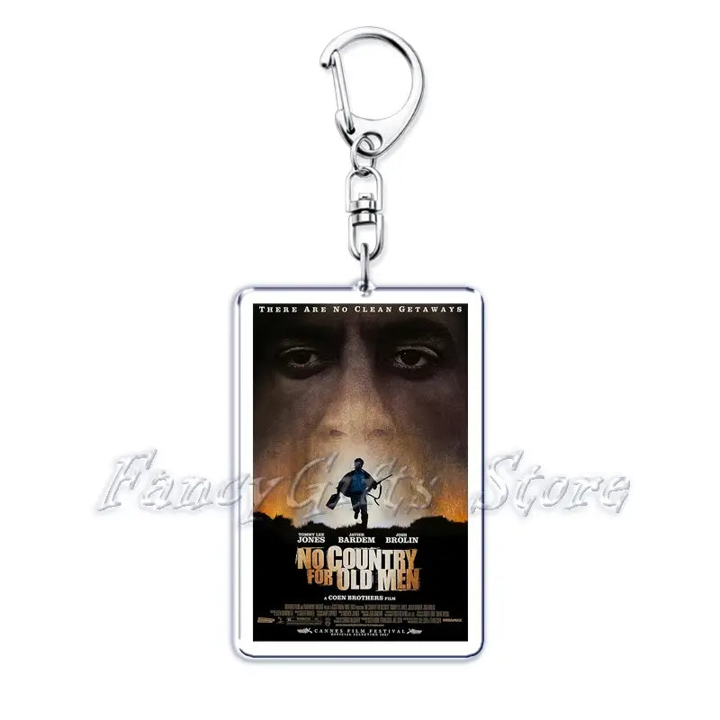 Silver rectangular acrylic keychain featuring a printed no country for old men movie poster with dark and warm tones showing a close-up face above a silhouette against an orange horizon.
