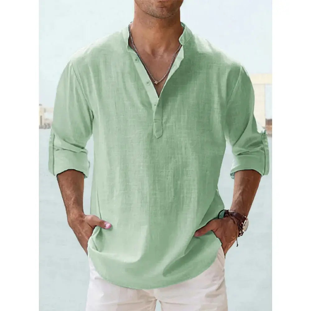 Chemise en lin henley à manches longues vert clair, avec patte boutonnée et poignets retroussés, conçue pour une tenue décontractée d’été à la plage.