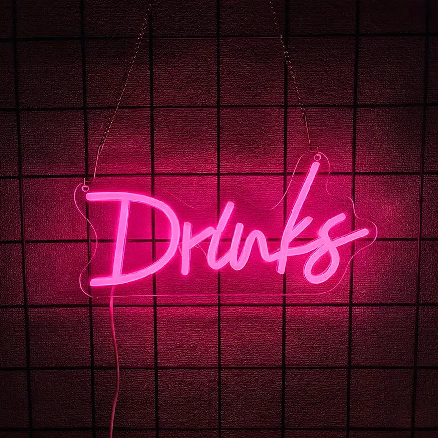 une enseigne au néon rose lumineuse formée comme le mot « drinks » dans un style cursif à LED, suspendue contre un mur sombre à motif de grille, comme décoration murale
