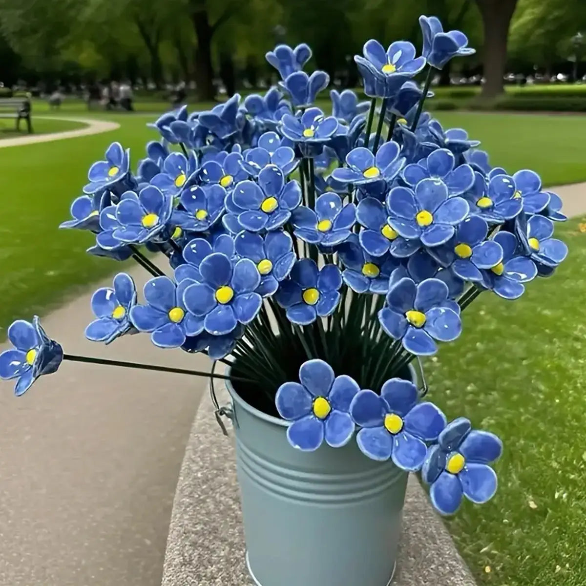 a bouquet of vibrant blue ceramic artificial flowers shaped as forget-me-nots with yellow centers arranged in a light gray metal bucket for decorating vases